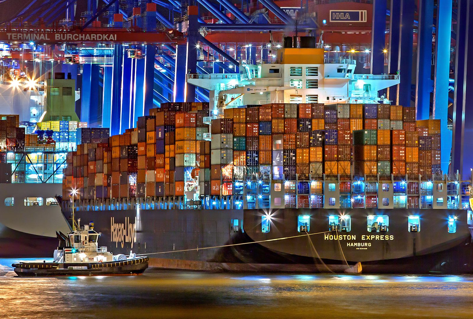 Container ship at a lit terminal with a harbour tug
